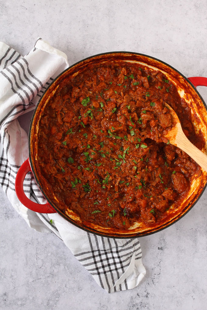 the lamb ragu sauce in a large red pop garnished with chopped basil