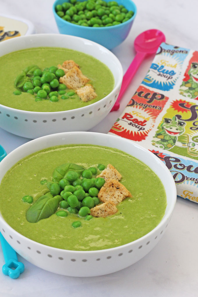 Green Spinach & Pea Soup in tow white bowls topped with fresh peas, basil leaves and croutons.