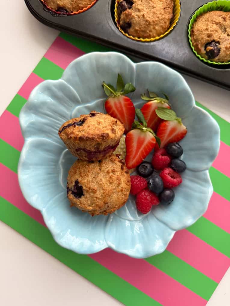 Two muffins in a baby blue,flower shaped bowl, served with fresh berries.