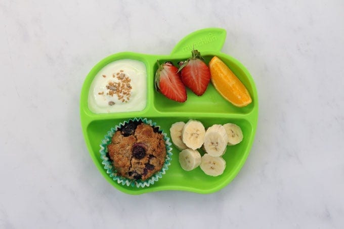 Blueberry Lemon Weetabix Muffins on a Munkin green plate topped with fresh chopped fruit, plain yogurt and seeds