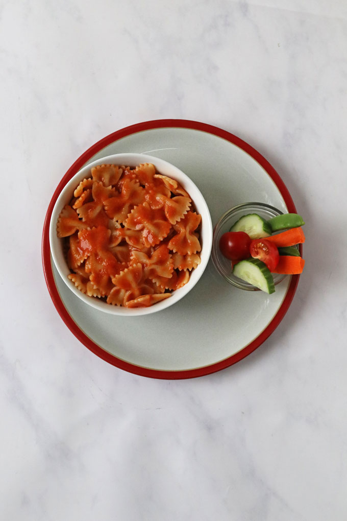 Hidden Veggie Tomato Sauce added to a bowl of pasta shapes, with a small bowl of chopped veggies on the side.