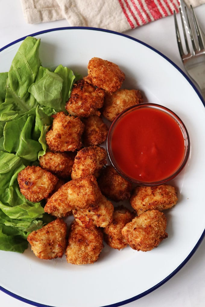 Homemade Chicken nuggets served on a white plate with a ramekin of ketchup and side serving of lettuce for garnish