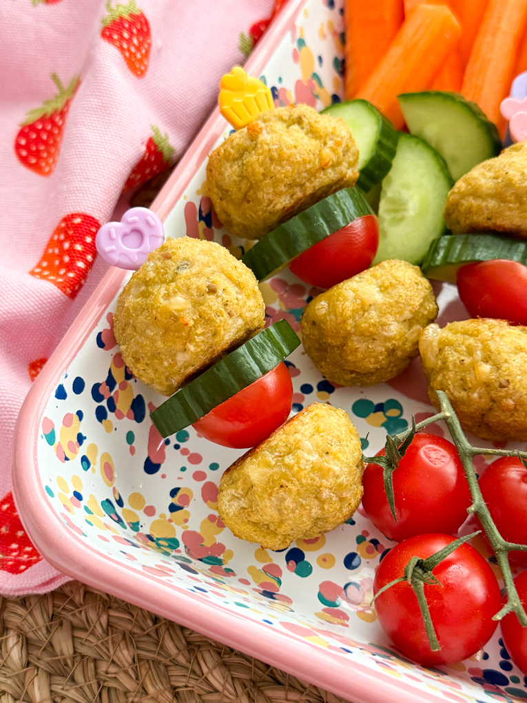 Easy chicken meatballs,cherry tomatoes and a slice of cucumber served on colorful pick sticks, served in a bright rectangle serving dish with chopped,fresh fruit & veggies.