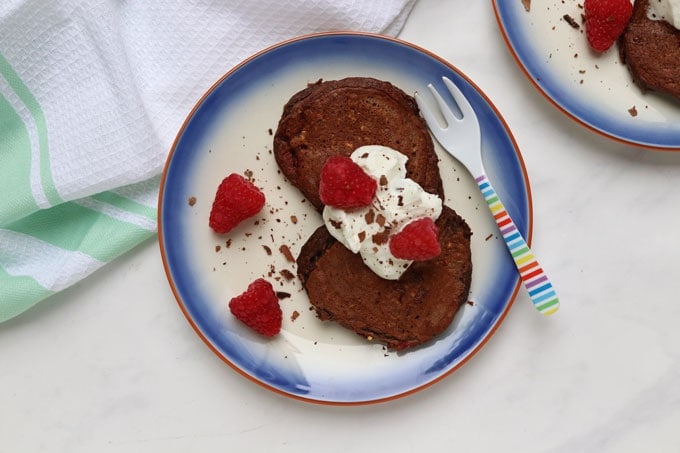 Easy Make-Ahead Breakfast Recipes & Ideas For Kids - Two plates of chocolate raspberry pancakes topped with a dollop of greek yogurt and fresh raspberries