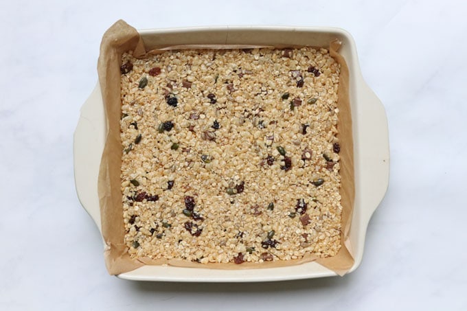 granola bar mixture in a square oven proof dish that is lined with parchment paper