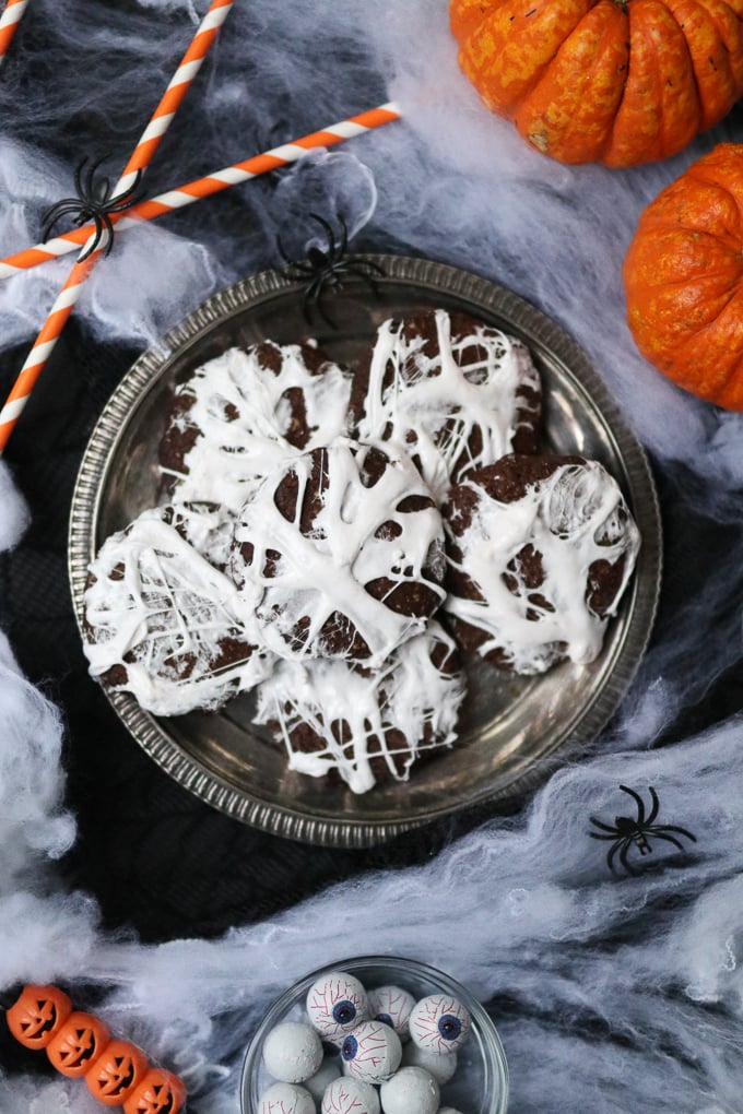 Fun Halloween Food Ideas For Kids -Chocolate Spider Web Cookies on a silver platter sat on spiders web with plastic spiders in the background.