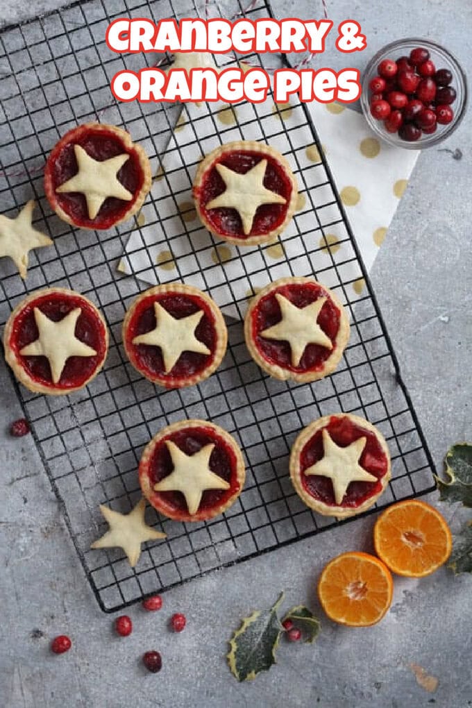 Cranberry & Orange Pies on a black wire cooling rack with fresh cranberries and orange halves surrounding the for decoration.