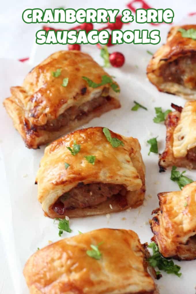 Cranberry and Bries Sausage rolls sat on top of white parchment paper, garnished with freshly chopped herbs.