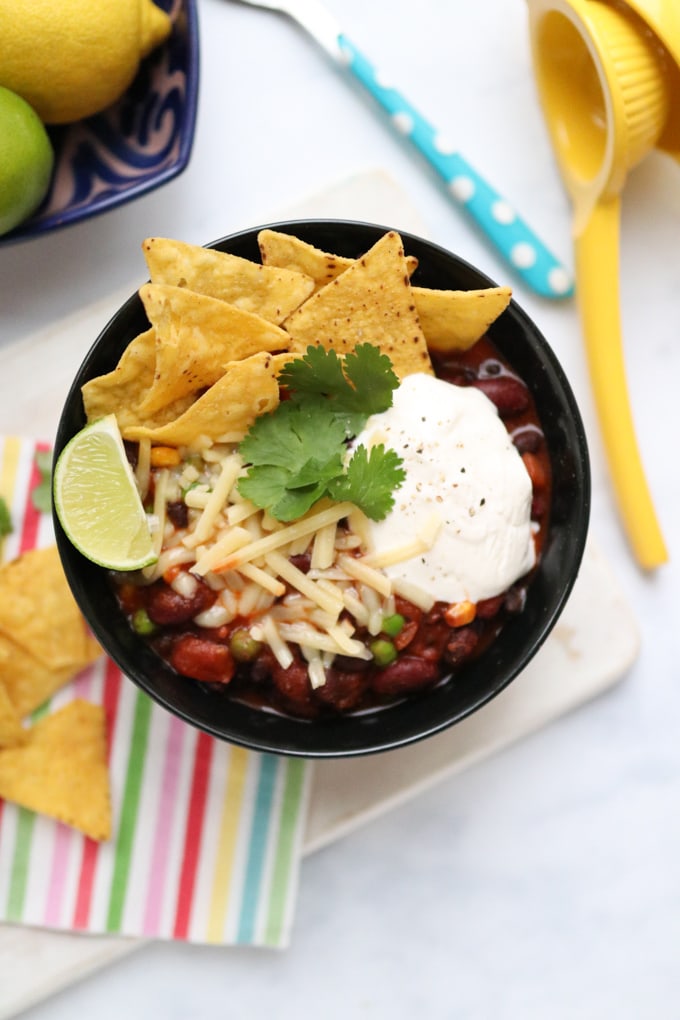 Smoky Bean Chilli in a Bowl with grated cheese, limed wedge and tortilla chips