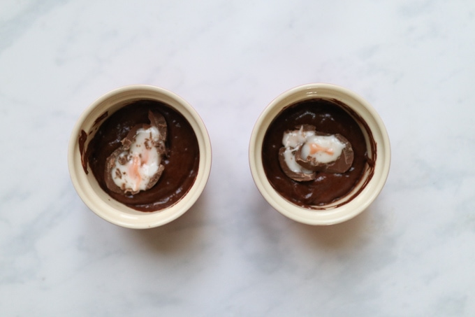 the creme egg mug cake mixture divided into two ramekins and topped with half a creme egg.