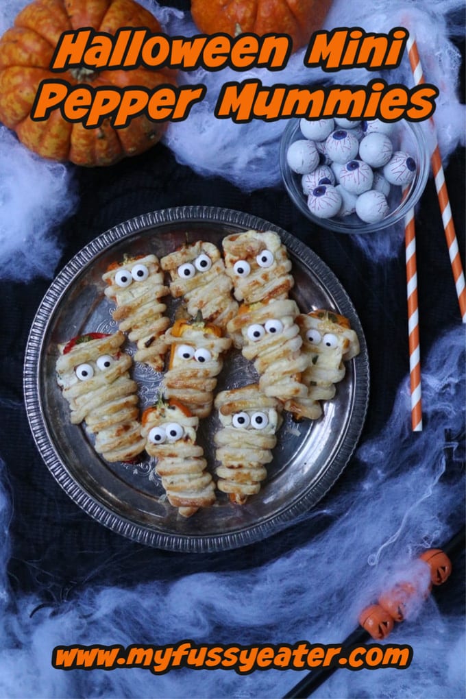 Stuffed Mini Pepper Mummies on a silver plate with spider web decorations in the background.