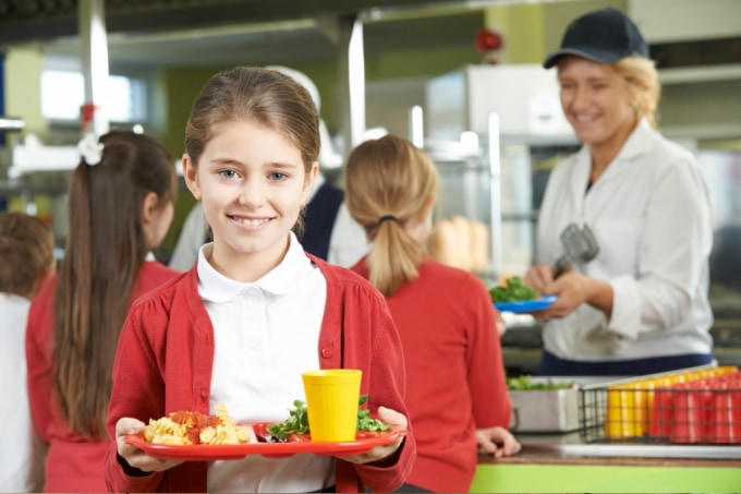 A school aged female child carrying a school lunch tray.