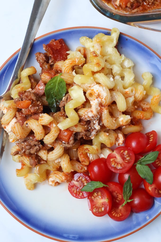 pasta bolognese bake served on a blue plate with a simple tomato salad on the side