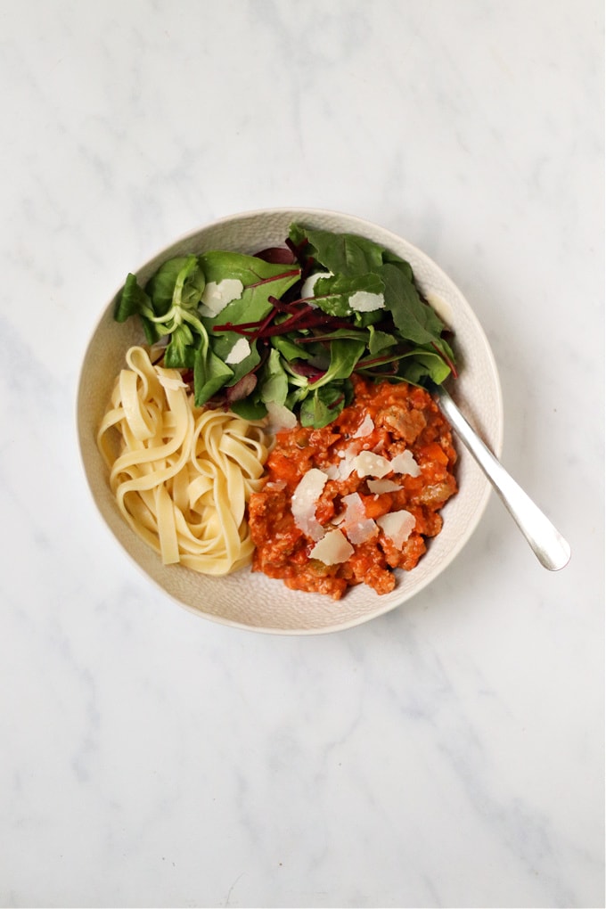 Turkey Sausage Ragu served in a white bowl and garnished with a side salad and parmesan shavings.