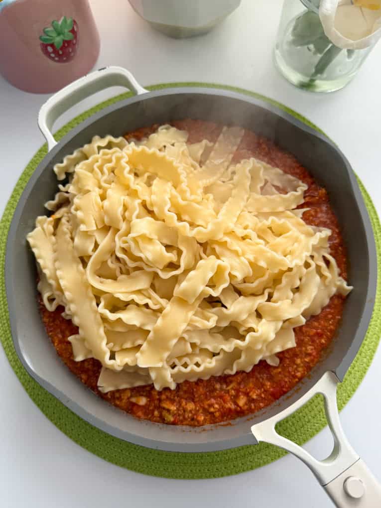 Pasta added to the ragu sauce in a saucepan.