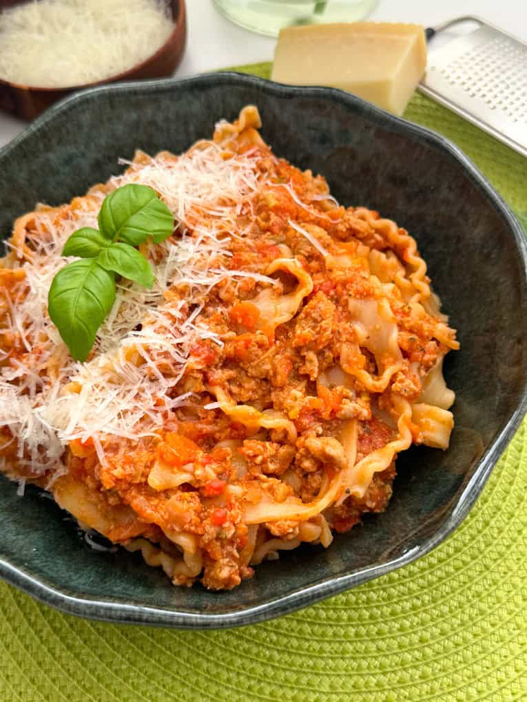 A bowl filled with turkey sausage ragu, garnished with grated cheese and basil leaves.