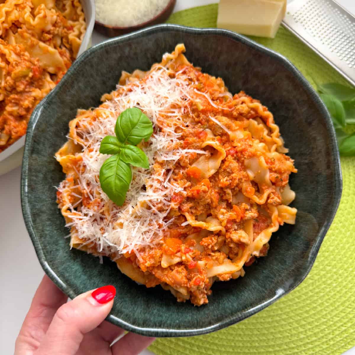 A bowl filled with turkey sausage ragu, garnished with grated cheese and basil leaves.