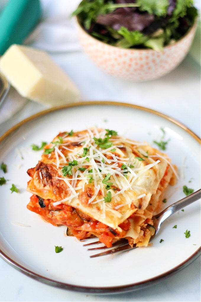Chicken lasagna served on a white dinner plate, and garnished with grated cheese.