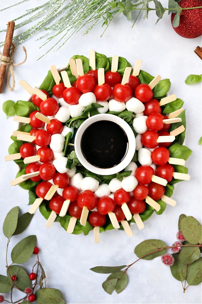 the finished Christmas caprese wreath with sprigs of eucalyptus leaves and red berries in the foreground