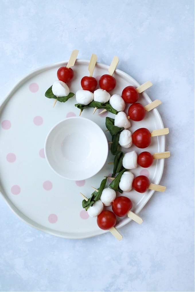 a round serving platter showing how to begin arranging the caprese skewers