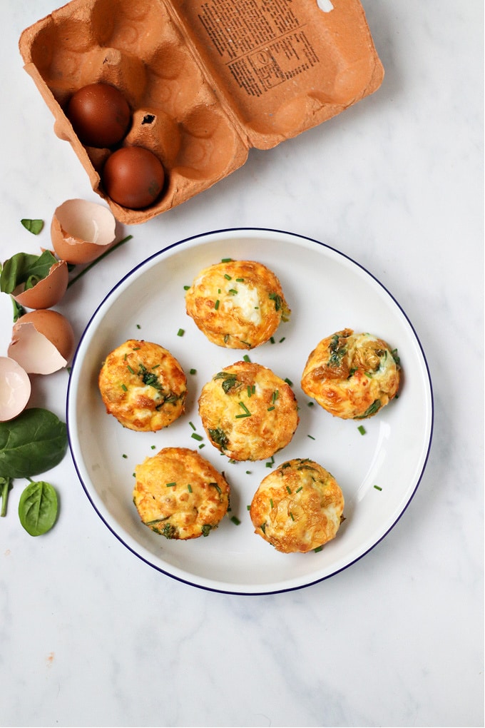 Delicious egg muffins flavoured with feta cheese and spinach. A tasty and healthy low carb lunch. served on a large round white dinner plate and garnished with chives.