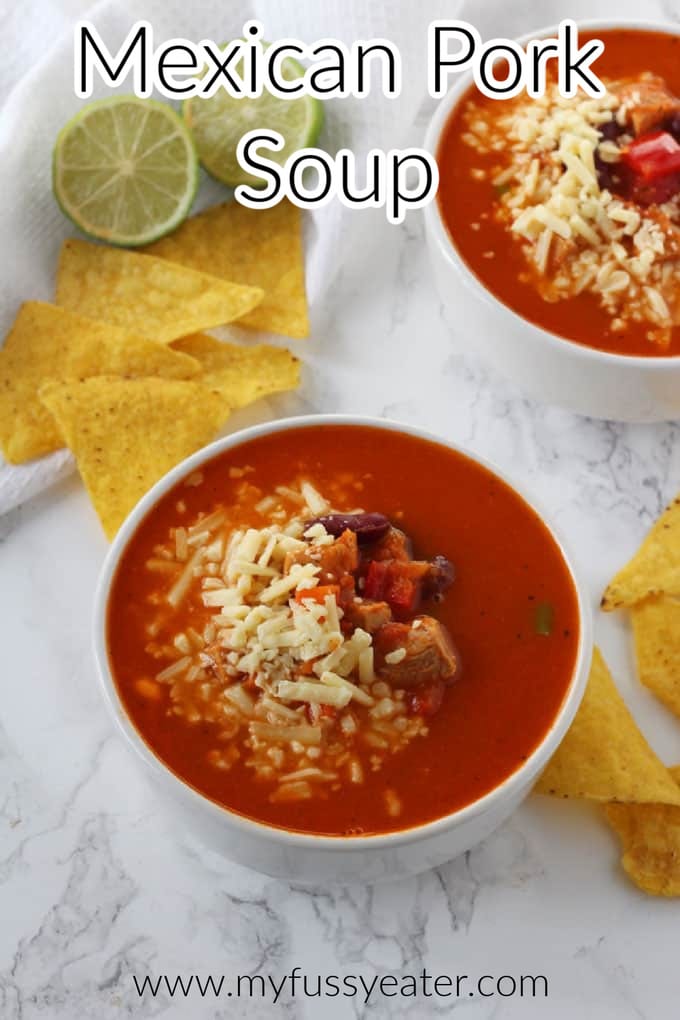 2 bowls of Mexican Pork Soup topped with grated cheese with tortilla chips and lime wedges in the background.