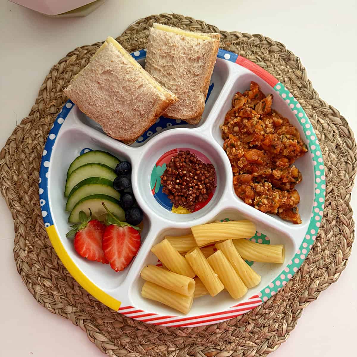 A midi pick plate full of different foods,including pasta bolognese, a cheese sandwich and sliced cucumber & strawberries.