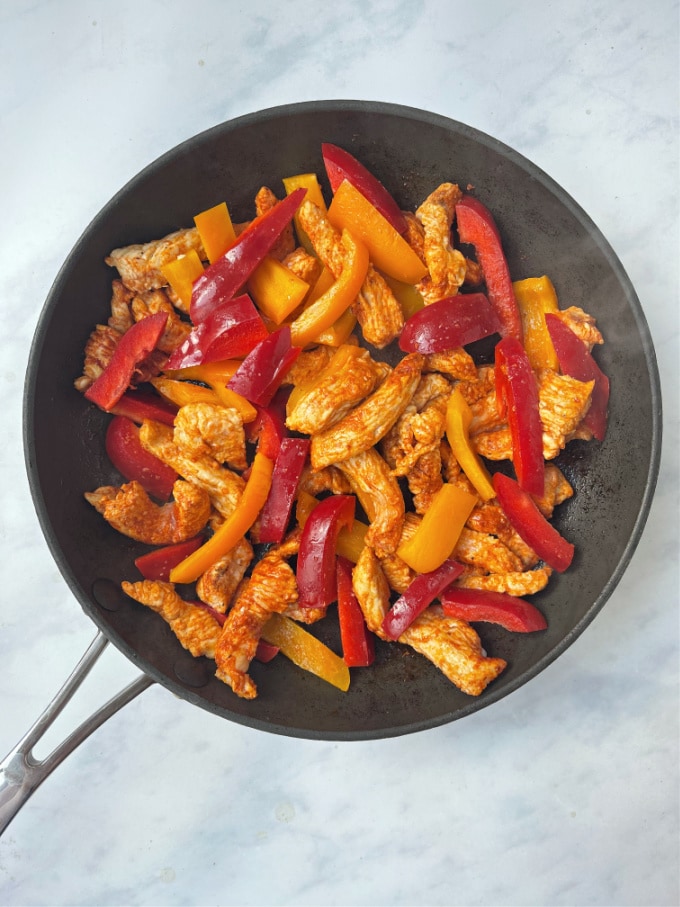 turkey strips in a frying pan with red and orange peppers