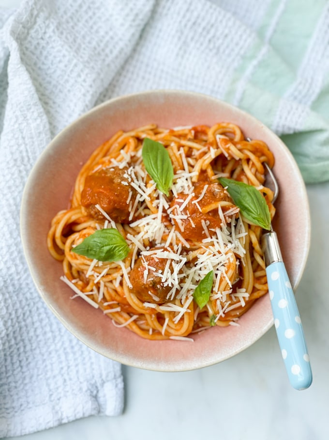 Slow cooker spaghetti meatballs in a bowl served with parmesan and basil leaves