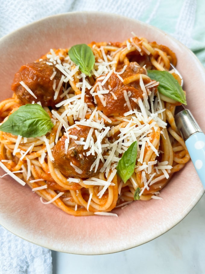 spaghetti meatballs served in a bowl topped with grated parmesan and fresh basil leaves