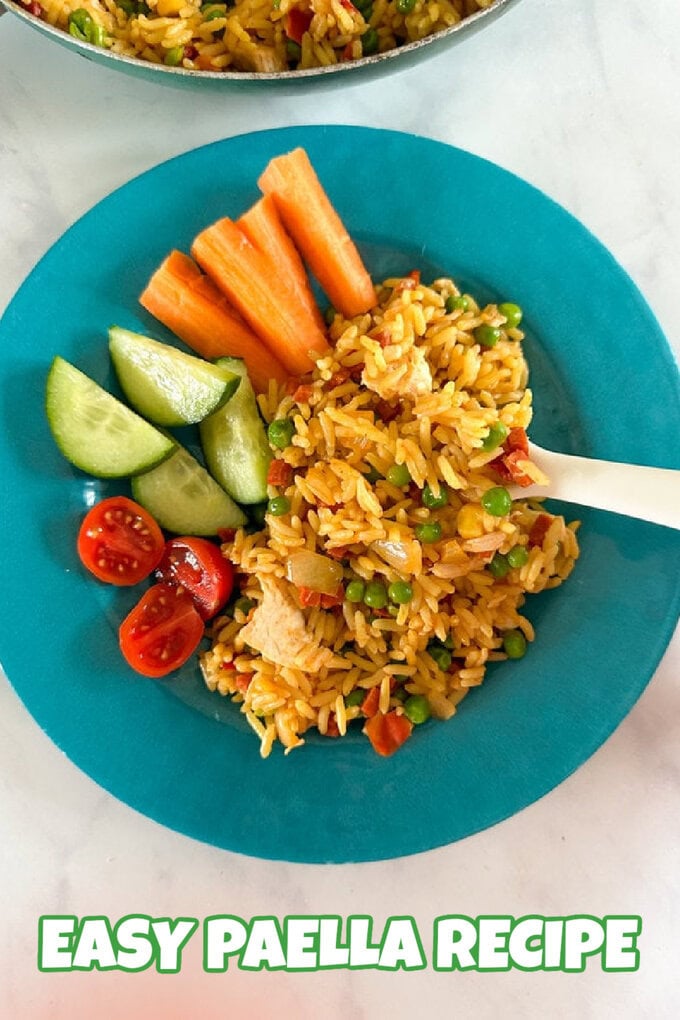 A serving of paella on a bright blue plate with a side serving of freshly chopped veggies.