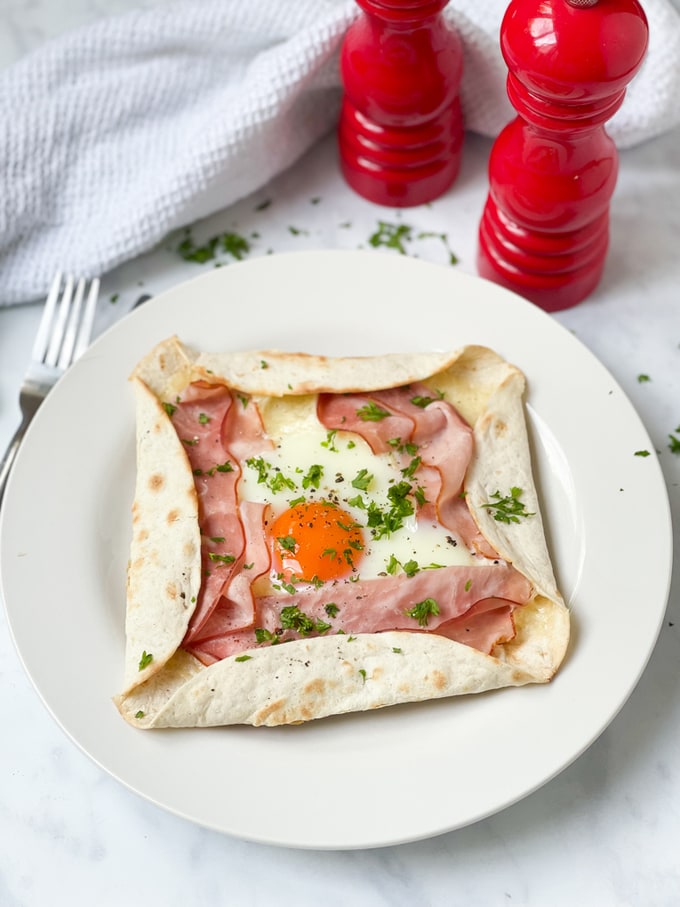 Cheat's Ham & Cheese Galette served on a white plate with red salt and pepper grinders in the background