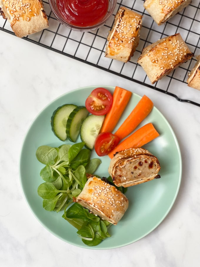 Chicken sausage rolls served on a light green plate with chopped veggies