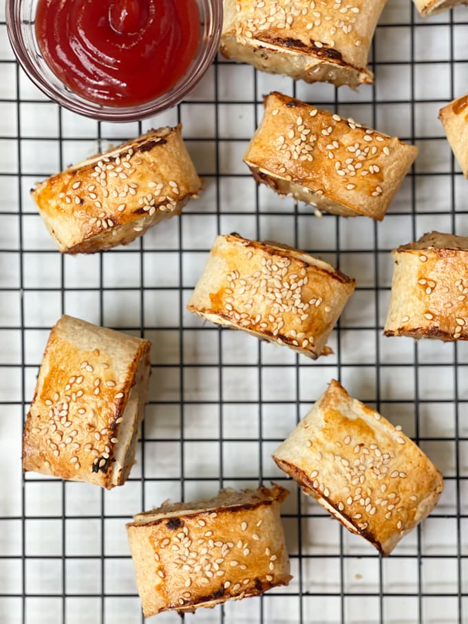 the cooked sausage rolls on a cooling rack with a small bowl of tomato sauce