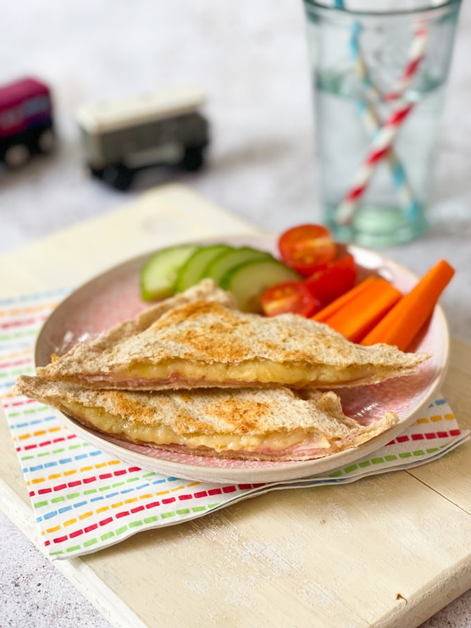 Cheese & Ham Toaster Toastie on a plate with cucumber, tomatoes and carrot batons