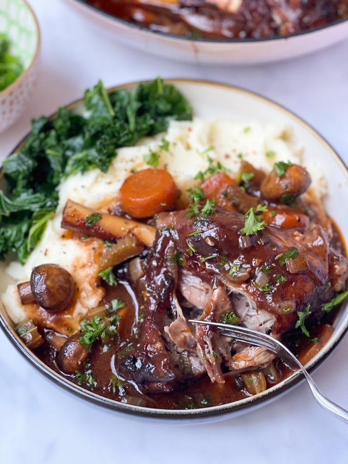 lamb shank casserole in a bowl with mashed potatoes and greens