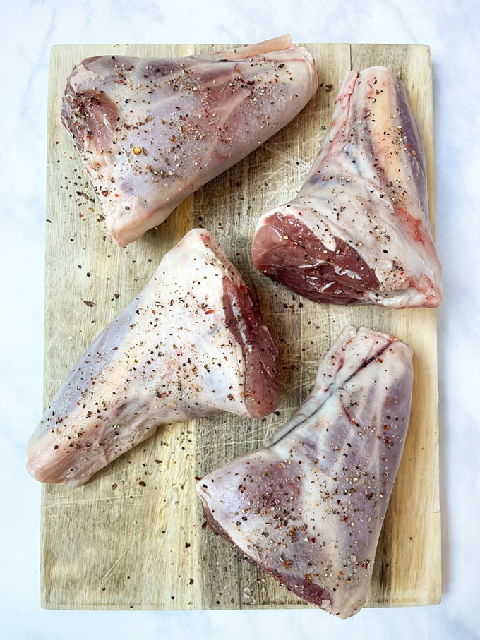 four seasoned lamb shanks on a wooden chopping board