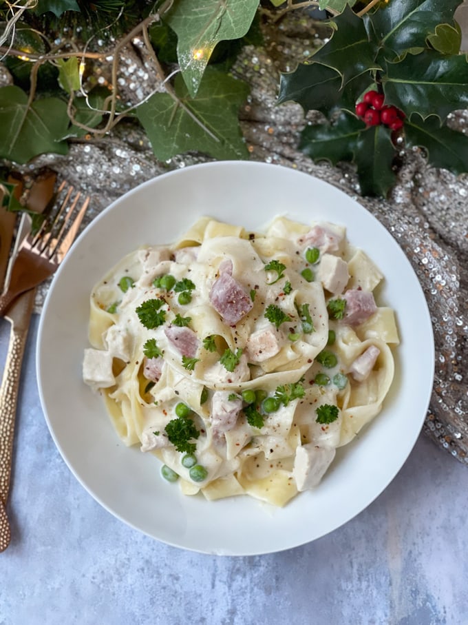 Leftover Turkey & Ham Pasta served in a white bowl with Christmas decorations in the background.