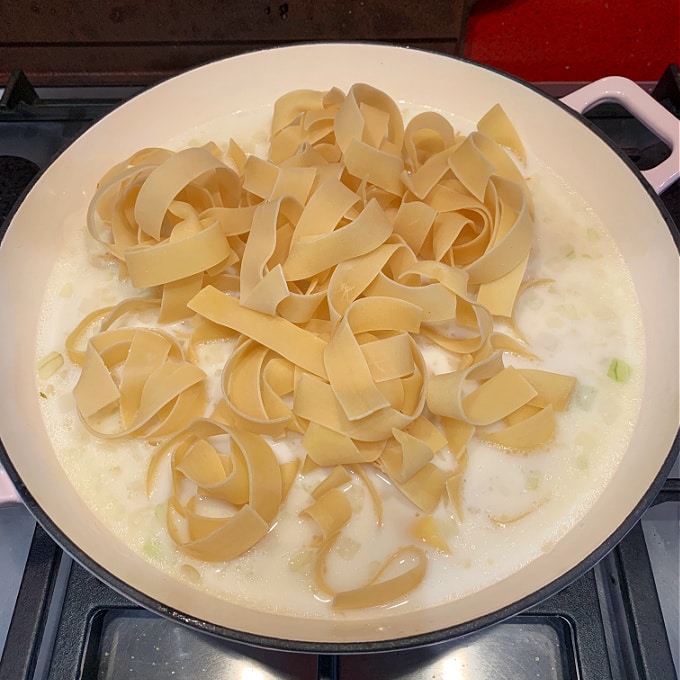 milk, chicken stock and pasta added to the onions in the pan on the hob
