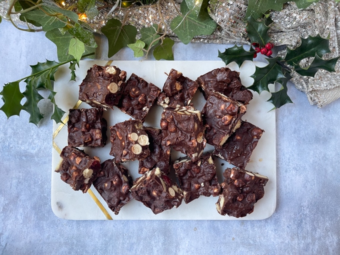 Mince Pie Rocky Road cut into squares on a white marble workbench with holly and christmas lights in the background.