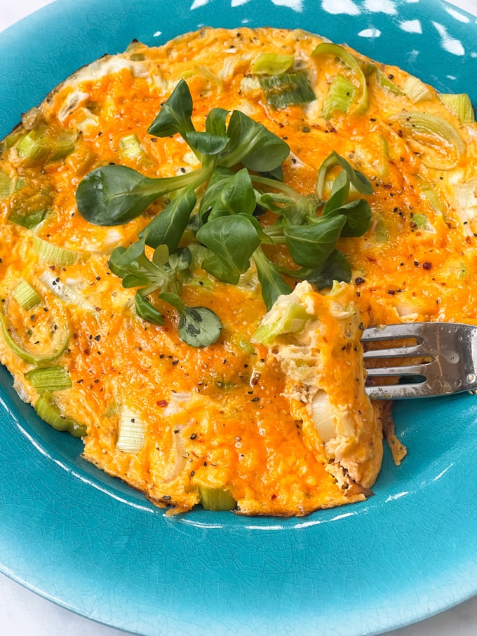 cheesy leek omelette served on a blue plate and garnished with pea shoots