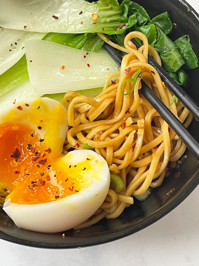 Hot oil noodles with pak choi and egg served in a brown bowl and topped with chilli flakes.