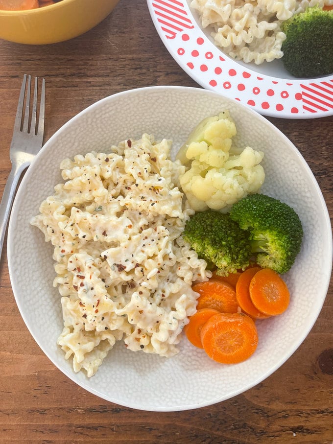 Boursin pasta served in a white bowl with carrots, broccoli and cauliflower