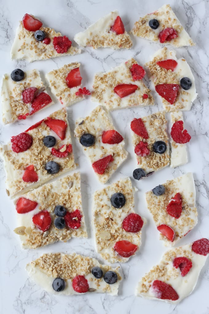 Breakfast frozen yogurt bark broken into pieces on a white marble background