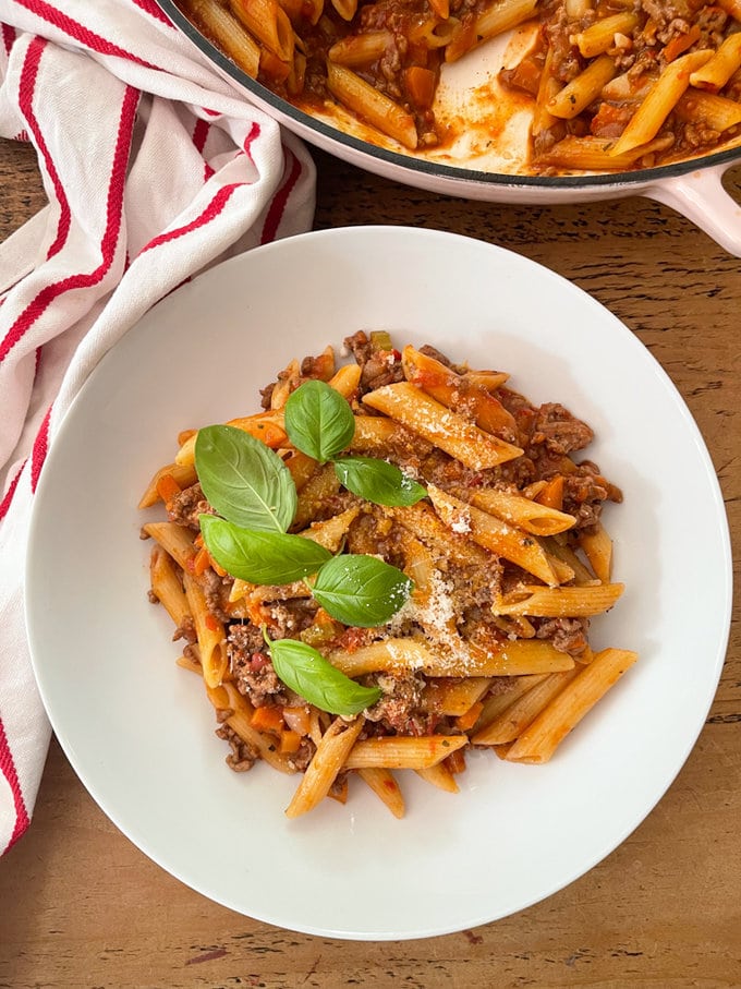 One Pot Pasta Bolognese served in a white bowl garnished with fresh basil leaves and grated parmesan cheese
