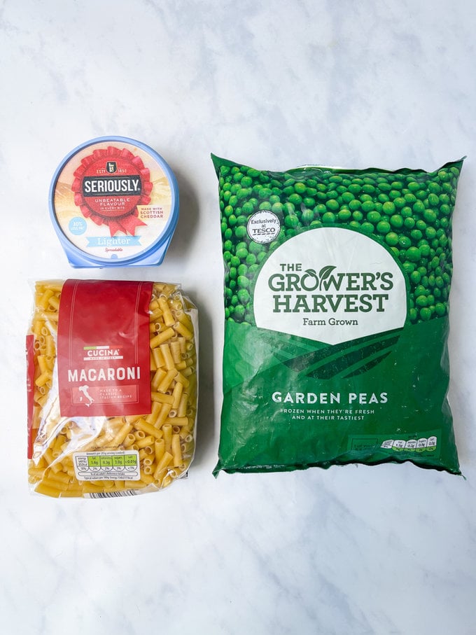 Cream cheese, Macaroni pasta and frozen peas laid out on worktop.