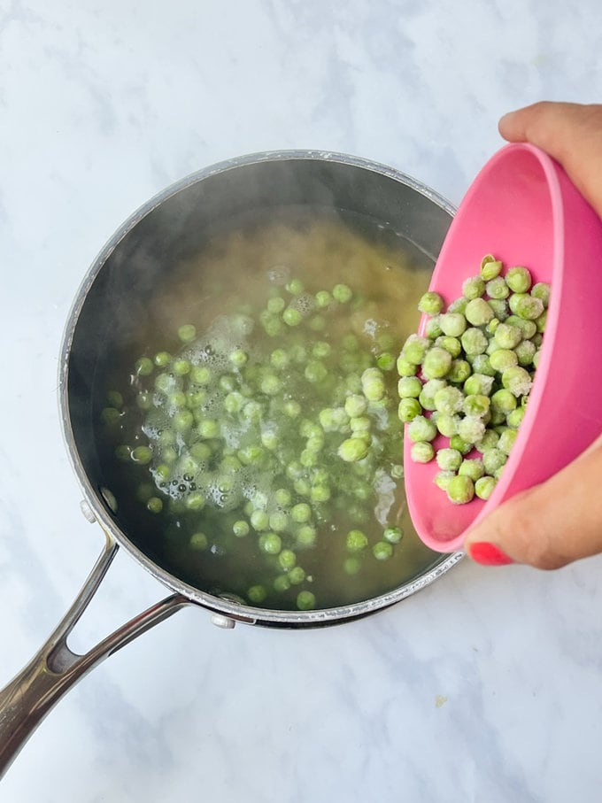 Frozen peas being added to a pan of boiling pasta.