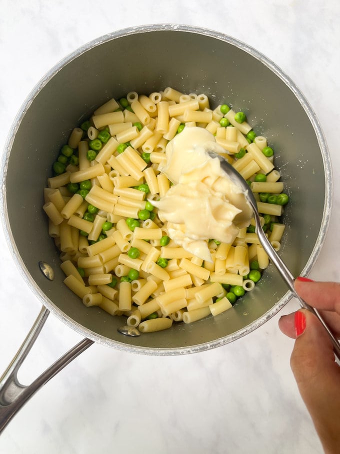 cream cheese being added to cooked pasta and peas.
