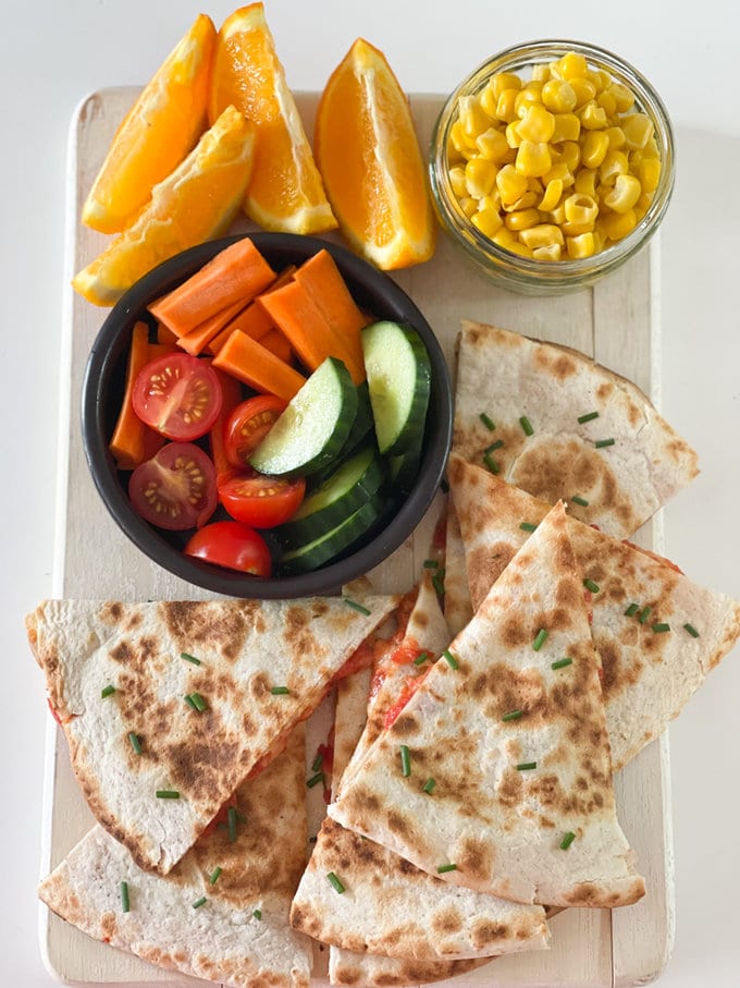 Cheese & Tomato Quesadilla, presented on a rectangle board along with a small bowl of Tomato's, cucumber and carrots