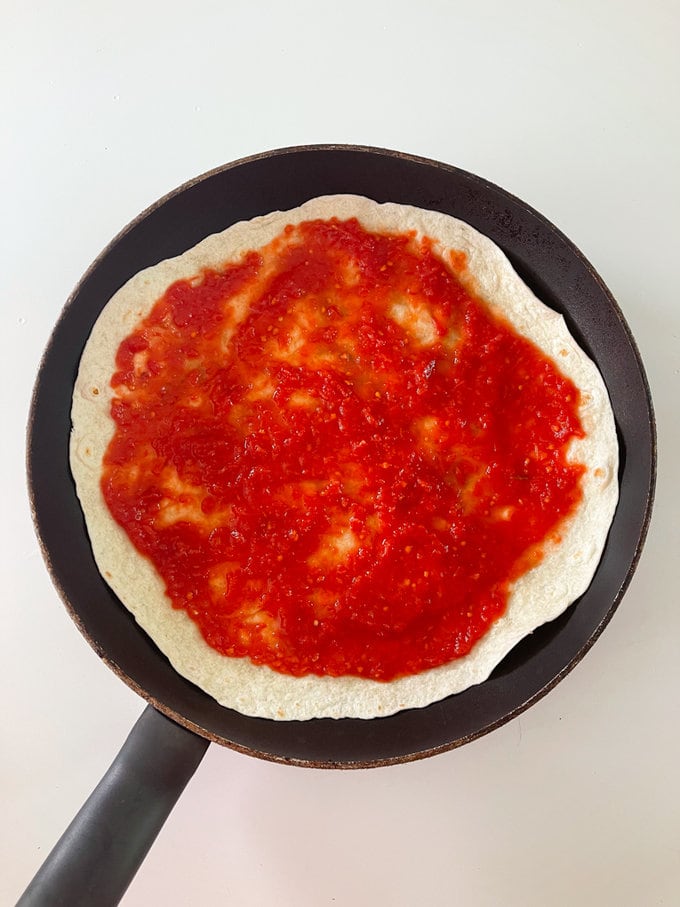 Tortilla wrap in frying pan with passata spread over the top.